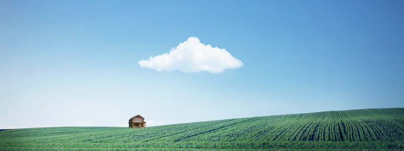 Huisje in een groen weiland onder een blauwe lucht met een wolk